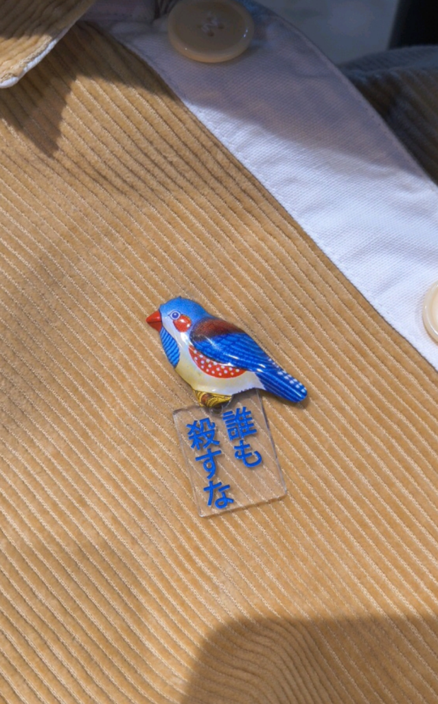 青い鳥のブローチに「誰も殺すな」というアクリルチャームがついている