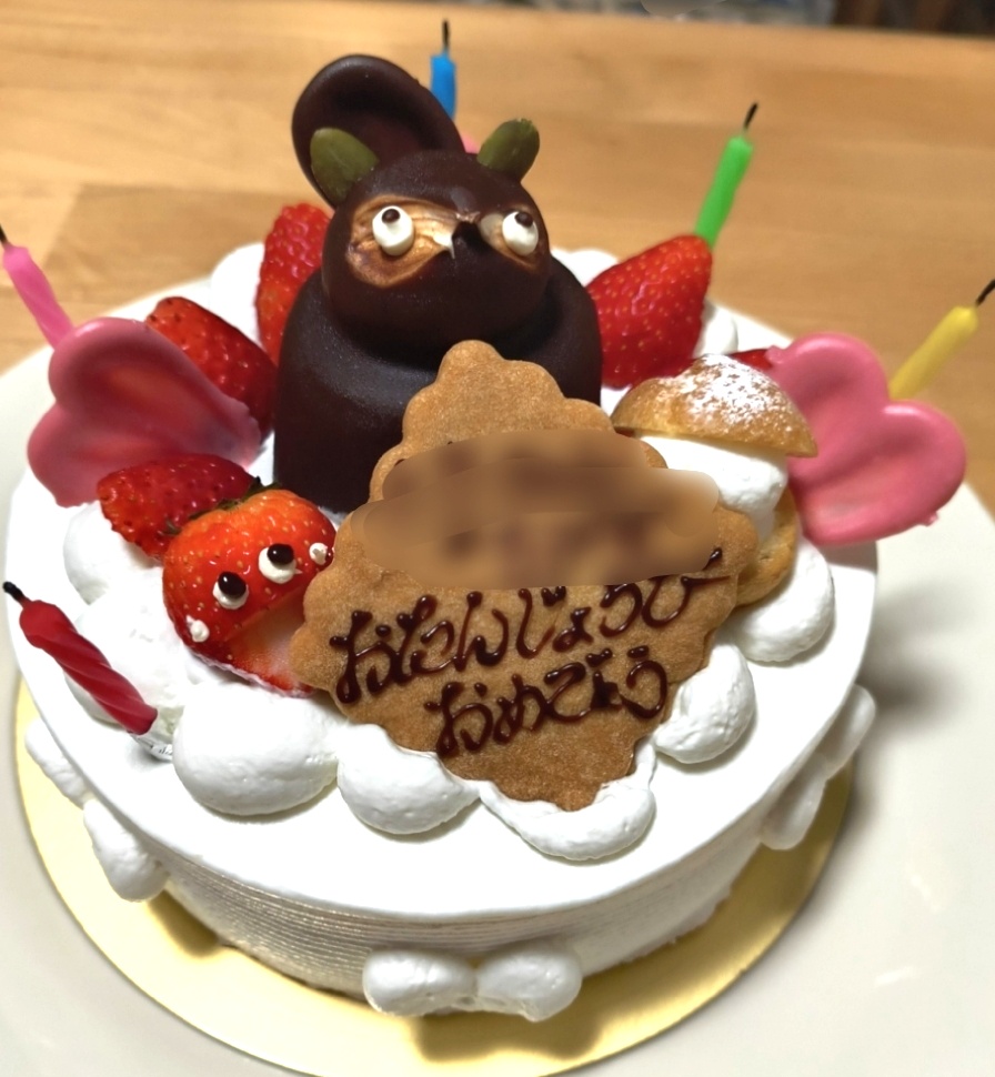 ホールの、ベージックないちごショートケーキの上に、茶色いたぬきの形をしたケーキと「おたんじょうびおめでとう」のクッキーが乗っている。